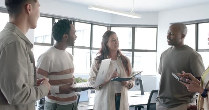 Diverse team meeting, striped man lifting laptop and sharing slides, moderator noting at office