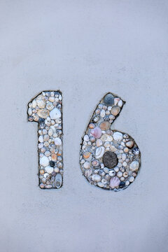 Number sixteen made with sea shells for address label on house. Number on light blue painted background