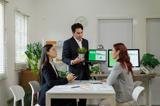 Business professionals are meeting in an office, discussing environmental, social, and governance strategy, with a presenter holding a plant and showing esg data on a laptop for sustainable growth