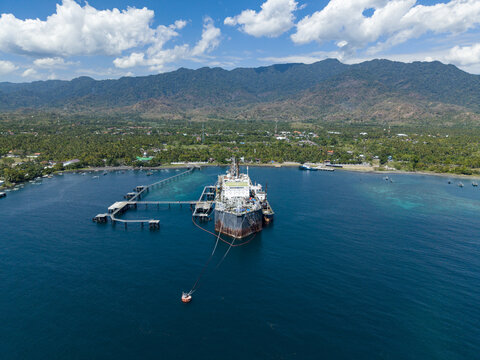 Aerial view of a Floating Storage and Offloading Ship moored at a pier in the coastal waters with lush mountains in the background in Buleleng Regency, Bali, Indonesia.