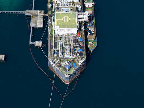 Aerial view of a Floating Storage and Offloading ship moored at a jetty with a helipad on deck and surrounding deep blue sea waters in Buleleng Regency, Bali, Indonesia.