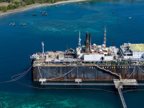 Aerial view of the Tuban Marine Terminal floating storage and offloading ship anchored in the clear blue waters with small fishing boats nearby in Buleleng Regency, Bali, Indonesia.