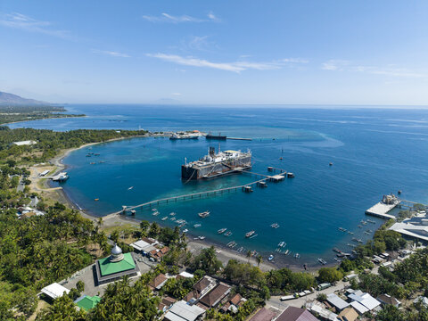 Aerial view of a Floating Storage and Offloading Ship FSO anchored in the bay, surrounded by coastal vegetation, fishing boats, and a nearby mosque in Buleleng Regency, Bali, Indonesia.