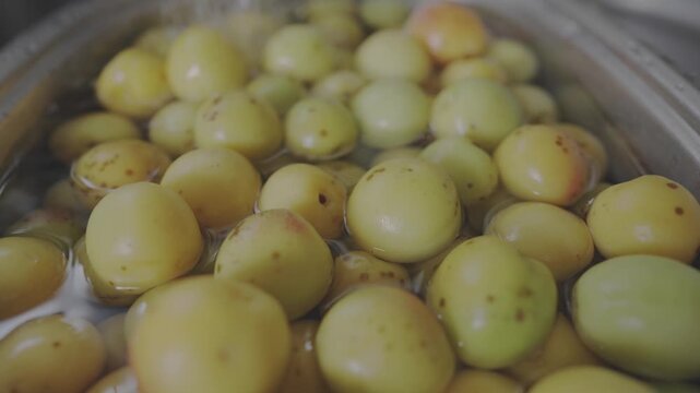 Close-up shot with depth of field showing organic Japanese plums soaked in water for homemade umeboshi