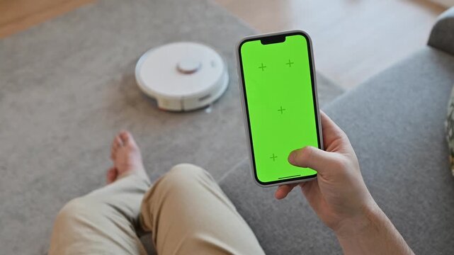 Man uses smart phone app with green screen to turn on smart vacuum cleaner 