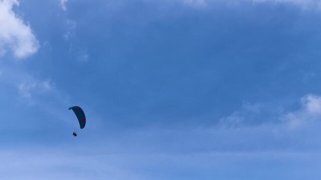Paraglider Soaring High Across Clear Blue Sky With Soft White Clouds