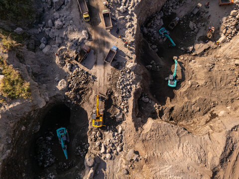 Aerial view of a busy stone quarry with excavators and dump trucks loading rocks and earth in Klaten, Central Java, Indonesia.