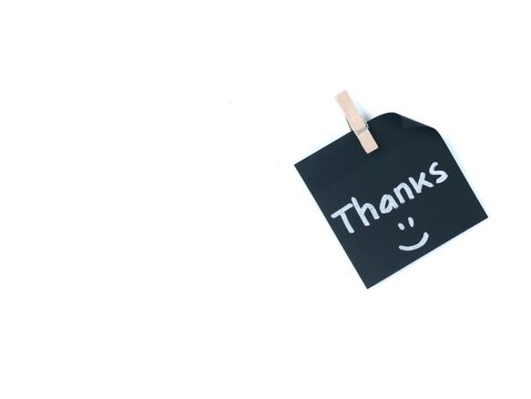 Thanks handwritten with happy face on a black adhesive note clipped with wooden peg, isolated on white background. Minimalist design for customer appreciation, gratitude, and friendly notes