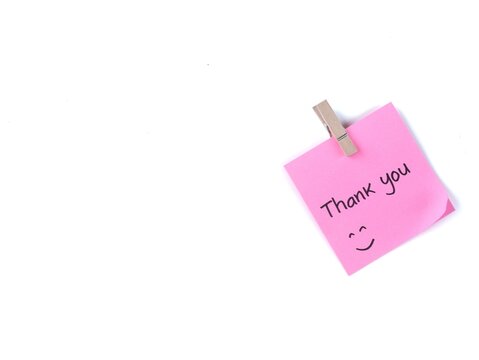 Thank you handwritten with happy face on a pink adhesive note clipped with wooden peg, isolated on white background. Minimalist design for customer appreciation, gratitude, and friendly notes