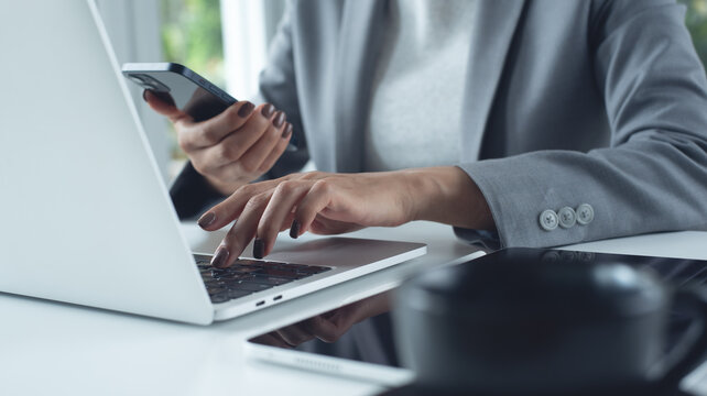 Business woman working in modern office, using laptop and smartphone surfing the net on office desk, close up