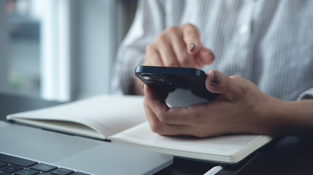 Close up of business woman using mobile phone with laptop on office desk, working in modern office
