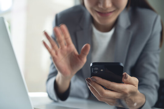 Asian business woman using smartphone for video call during working with laptop on office desk, modern lifestyle