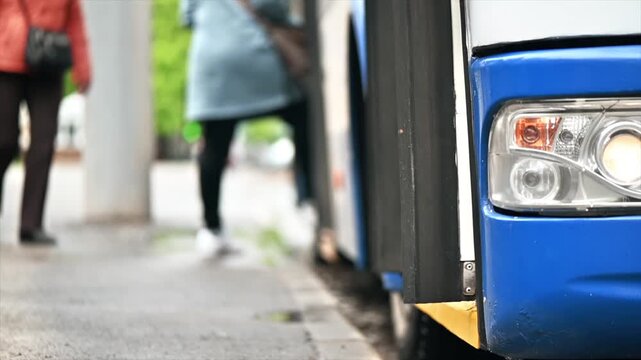 People boarding and exiting a city bus at a bus stop during the day passengers feet close-up entering and leaving public transport.