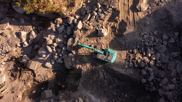 Aerial view of an excavator working in a rocky quarry with large boulders and earth, Klaten, Central Java, Indonesia.