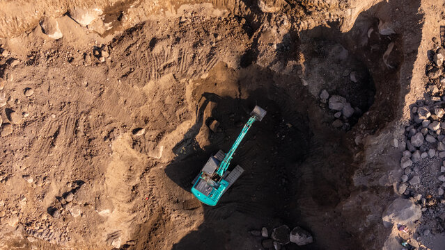 Aerial view of an excavator working in a large quarry with rocky terrain and excavated earth in Klaten, Central Java, Indonesia.