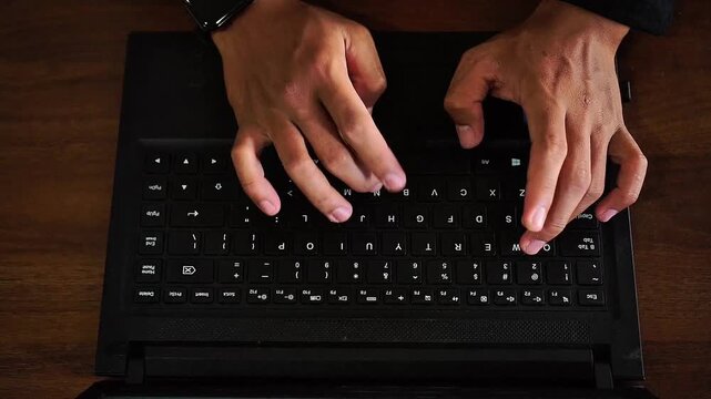 Close-up overhead view of human hands rapidly typing on a sleek, black laptop keyboard in a focused work environment, demonstrating productivity and digital engagement