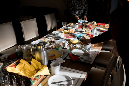 Sunlit family breakfast table with used dishes, coffee, bread and assorted foods after shared morning meal, authentic home lifestyle, togetherness and everyday domestic routine