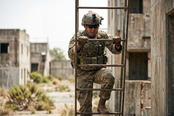 Fototapeta premium Asian male soldier in camouflage uniform climbs a metal ladder in a ruined urban environment