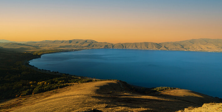 Landscape photograph of Lake Sevan surrounded by golden hills at sunset in Armenia.