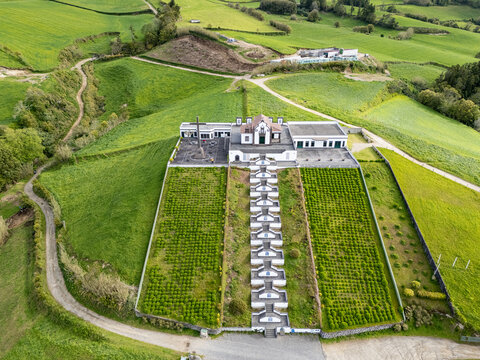 Aerial view of the Chapel of Nossa Senhora da Paz with its iconic staircase, surrounded by lush green hills and agricultural fields in Vila Franca Do Campo, Acores, Portugal.