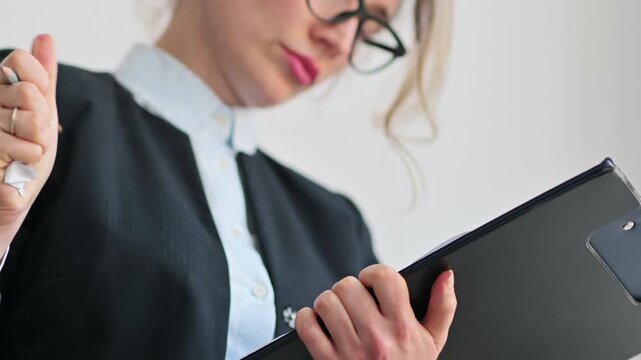 Businesswoman holding clipboard and writing notes on paper during daily office administrative tasks.