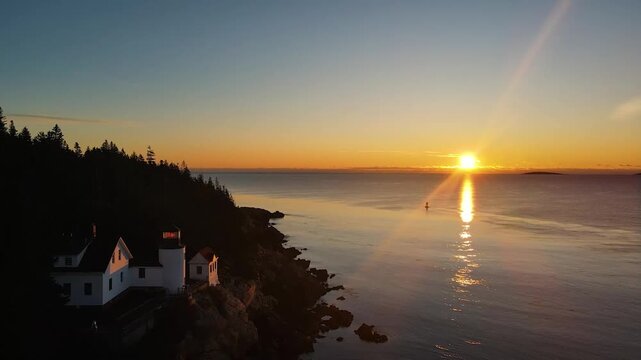 Golden sunrise light glows over the iconic Bass Harbor Head Light Station in Maine