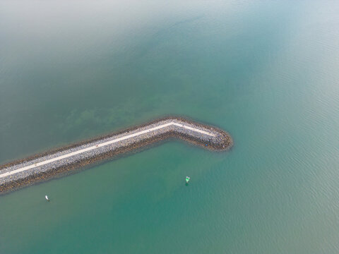 Aerial view of a stone breakwater in turquoise ocean water