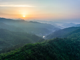 Fototapeta premium A serene landscape of layered forested mountains at sunrise, with mist drifting through valleys under a soft warm sky.