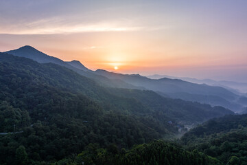 Fototapeta premium A serene sunrise illuminates layered forested mountain ranges with soft mist in the valleys and warm sky hues.