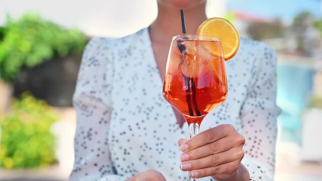 Woman holding orange spritz cocktail glass in outdoor setting during summer vacation.