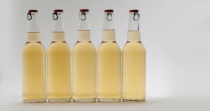 Perfect row of identical swing-top bottles filled with golden craft beer moving along a conveyor belt at a bottling plant, shown in slow motion against a clean, isolated white background.