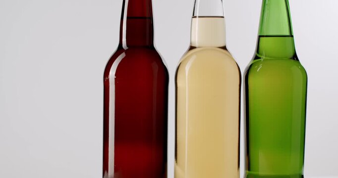 Various craft beer bottles rotating in slow motion, isolated on a white background. Brown, green, and clear glass bottles featuring an assortment of pale ales, lagers, and ciders