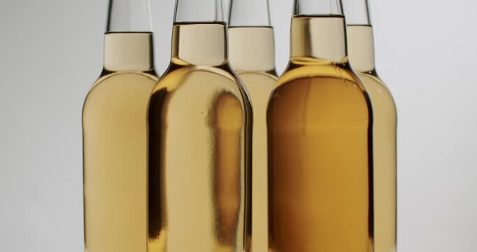 Perfect row of identical swing-top bottles filled with golden craft beer moving along a conveyor belt at a bottling plant. Clear glass bottles filled with fresh, unfiltered apple cider