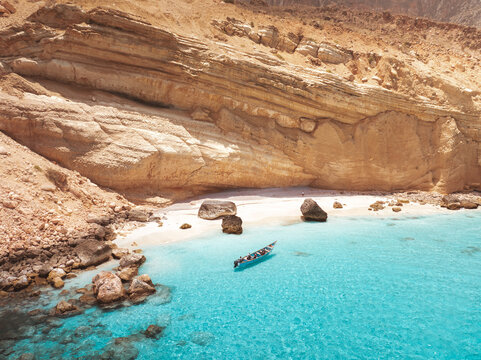 Aerial view of Shoab Beach with a small boat floating in the turquoise water near the rocky cliffs of Qalansiyah, Yemen.