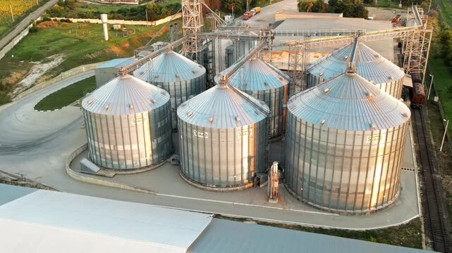 Aerial view of modern grain elevator storage facility with metal silos and railway tracks at sunset.