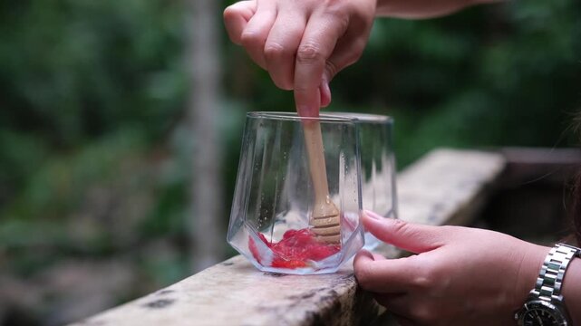 A woman squeezing raspberry in glasses and putting honey to make a drinks