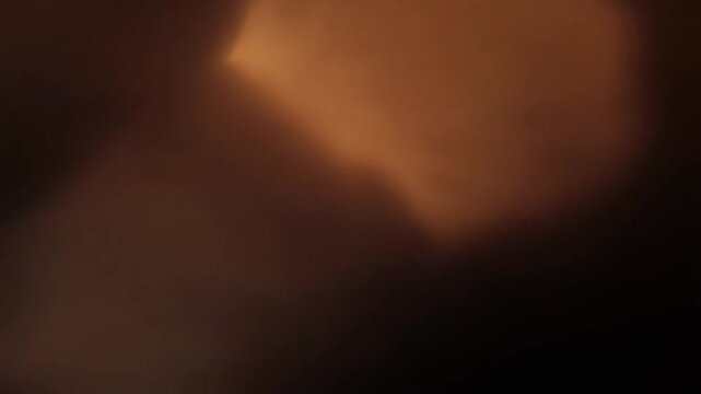 Warm amber light leak bleeds and spreads diagonally across a dark frame with soft organic edges, self-illuminated against total black &mdash; loop ideal for cinematic, retro, and film overlays.