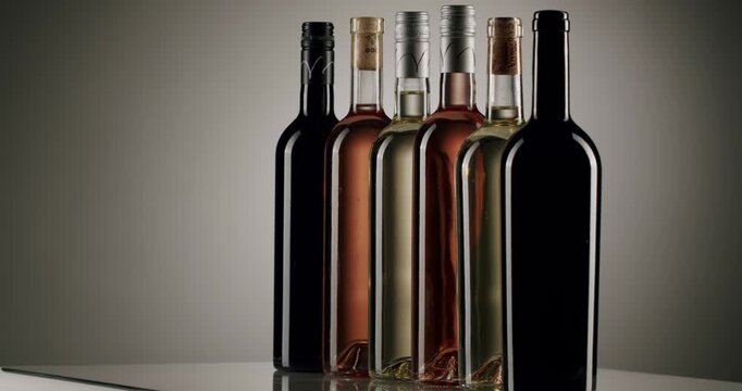 Assortment of red, rose, and white wine bottles with screw caps and cork stoppers appearing one by one in a line against a neutral background, highlighting the variety of winery production.