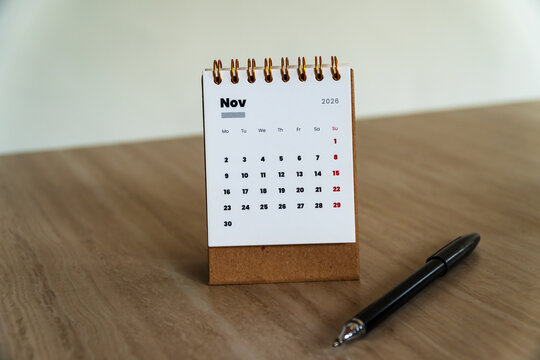 November 2026 mini desk calendar with a black pen on a light wooden surface. Front view layout for workspace planning and business setup concept.