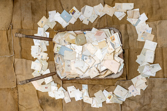 a collection of vintage, possibly antique, letters and envelopes, The letters are densely packed into a old wheelbarrow on a burlap backdrop