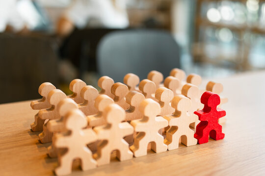 Standing out leadership concept with unique red wooden figure standing among crowd of neutral wooden figures on desk for business management, individuality, career success, and team growth.