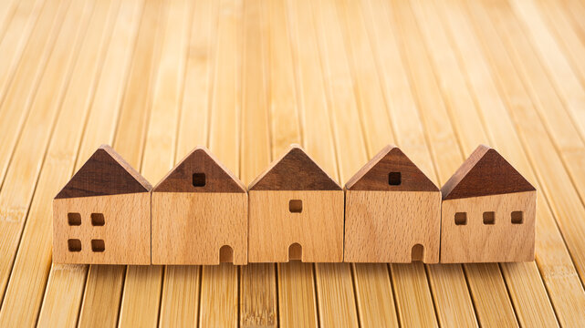 Real estate house models in a row on wooden background for property loan, home insurance, mortgage refinance, interest rate reduction, investment, debt planning, and housing market banner.