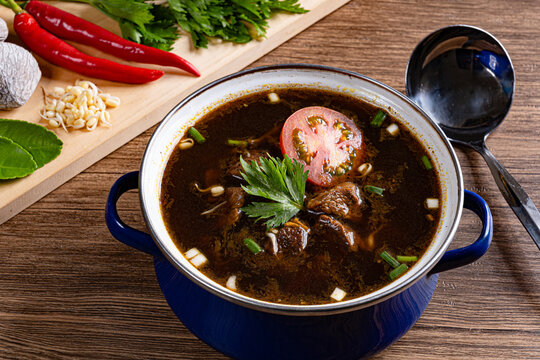 Traditional indonesian rawon beef black soup in blue pot with fresh spices and ladle