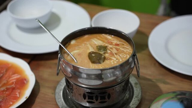 Hot and creamy Asian soup with enoki mushrooms served in a metal hot pot, showcasing comforting restaurant cuisine, spicy broth and fresh ingredients.