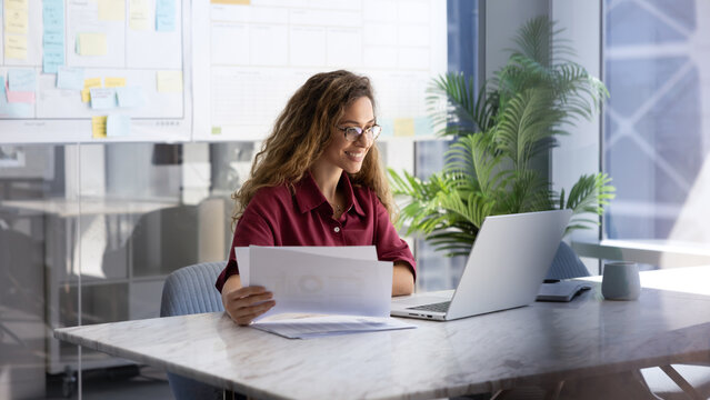 Businesswoman reviewing data, analyzing information, managing tasks, checking financial report, or preparing documents sitting at workplace desk with laptop. Business planning, professional workflow