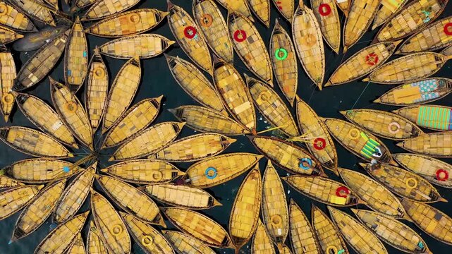 An aerial view captures traditional wooden commuter boats moored in a radial, flower-like pattern on the Buriganga River in Dhaka, Bangladesh.