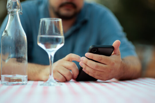 Close up of a Man Using His Smartphone At Restaurant Table. Focused guy browses online on a mobile phone during dinner outdoors 