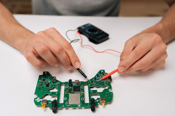 Repairman hands troubleshooting game controller circuit board with multimeter, checking electronic components and diagnosing potential issues during the repair and maintenance process. © dikushin