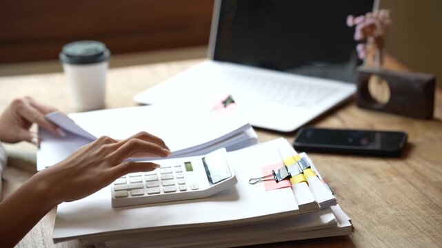 Business professional working on a laptop while managing stacks of organized documents and paperwork in a bright modern office.