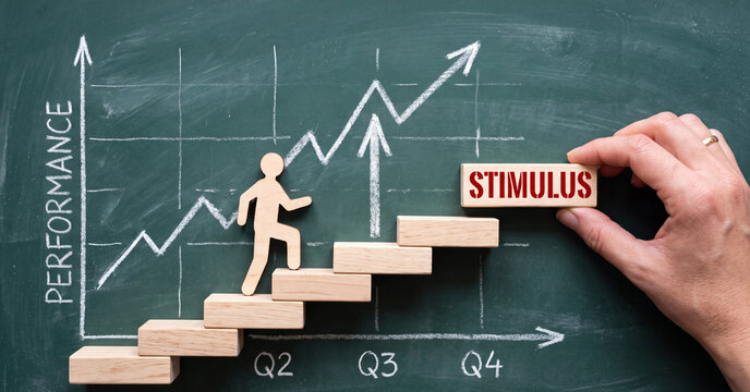Stimulus business concept depicted by wooden human figure climbing stair blocks on green chalkboard background with white chalk performance growth chart and hand placing block
